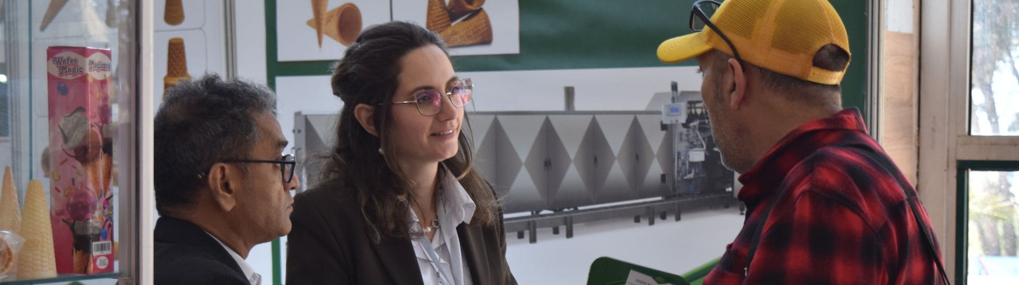 Trois personnes engagées dans une discussion à un stand d'exposition, avec des cônes de glace et des machines exposés en arrière-plan