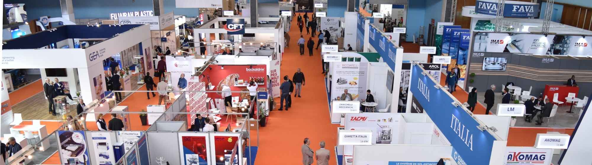 Aerial view of a trade show with multiple booths, orange carpeted walkways, and attendees exploring exhibits.