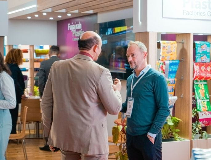 Two men are conversing at a booth at the Djazagro trade show, surrounded by displayed products and other visitors in the background.